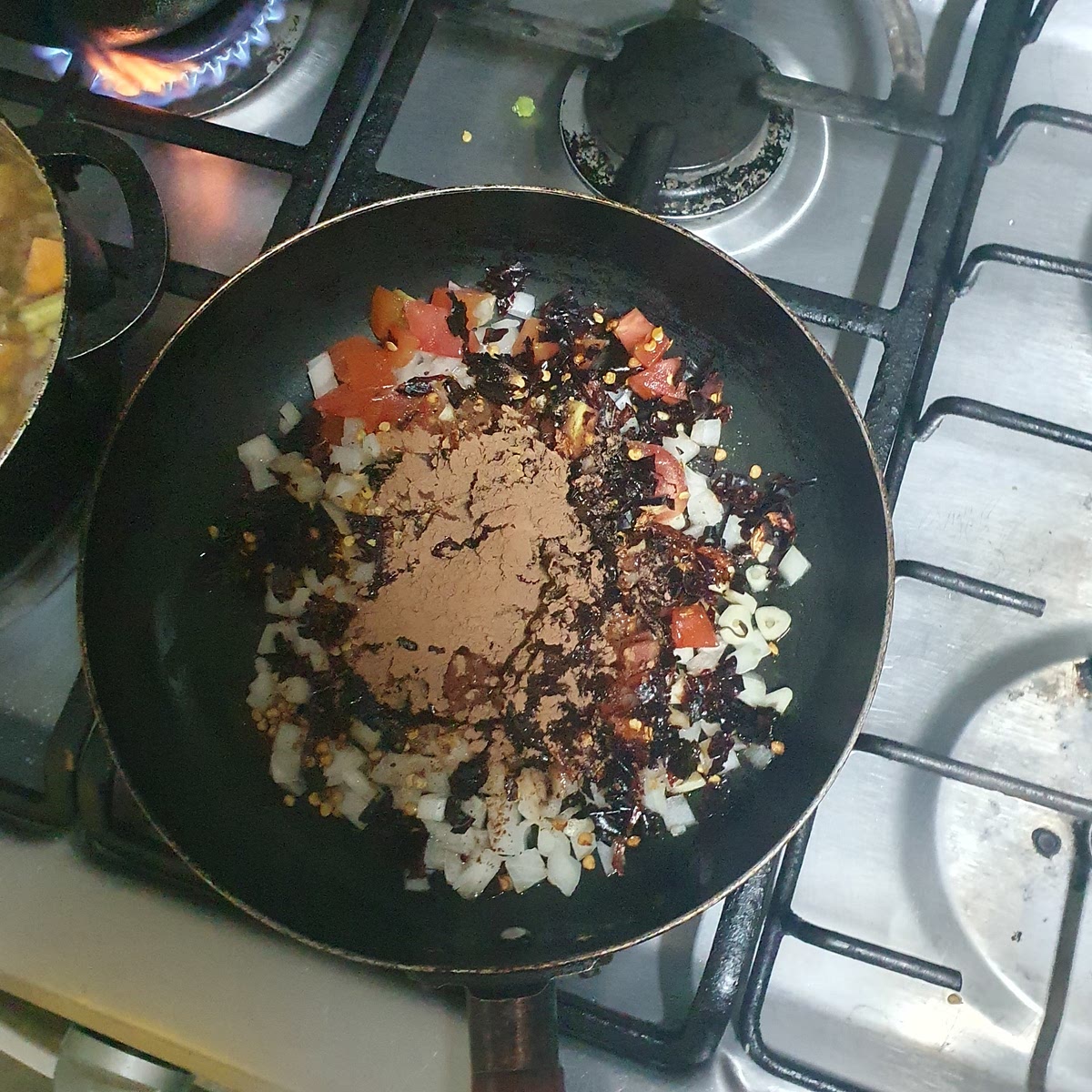 Snij de ui en tomaat in kleine blokjes blokjes (ong 0.5 cm x 0.5 cm) en snij de knoflook in reepjes. Voeg dit samen met de chilipeper, cacao poeder, tamarindepasta, en zwarte peper toe aan een pan met zonnebloemolie en myoteer op laag vuur tot de ui goud bruin is.