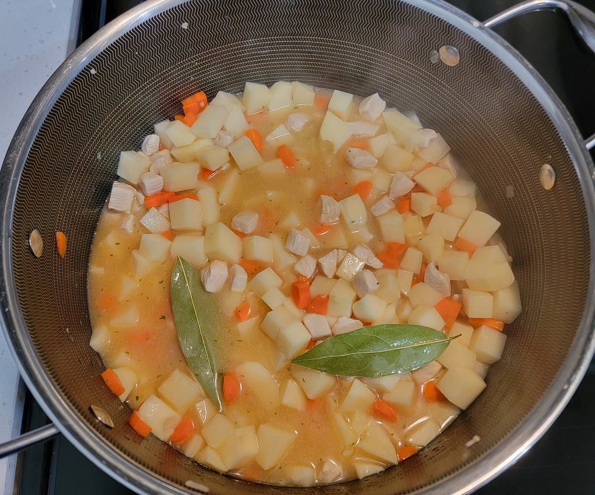 3. Once the chicken is mostly cooked, add the diced potatoes and carrots, along with the chicken broth and bay leaves. Cook on medium-high for 10-12 minutes, stirring frequently.