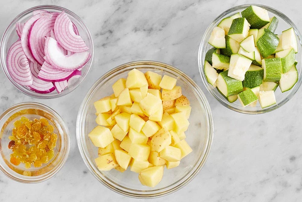 Remove the butter from the refrigerator to soften. Fill a medium pot 3/4 of the way up with salted water; cover and heat to boiling on high. Wash and dry the fresh produce. Medium dice the potatoes. Halve, peel, and thinly slice the onion. Medium dice the zucchini. Place the raisins in a bowl; cover with hot water. Set aside to rehydrate at least 10 minutes.