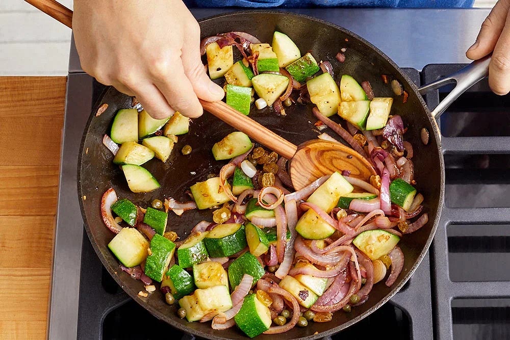 While the steaks rest, drain the rehydrated raisins (discarding the liquid). To the pan of reserved fond, add the sliced onion (if the pan seems dry add a drizzle of olive oil); season with salt and pepper. Cook, stirring occasionally, 2 to 3 minutes, or until slightly softened. Add the diced zucchini; season with salt and pepper. Cook, stirring occasionally, 4 to 5 minutes, or until browned and softened. Turn off the heat. Stir in the drained raisins and capers.