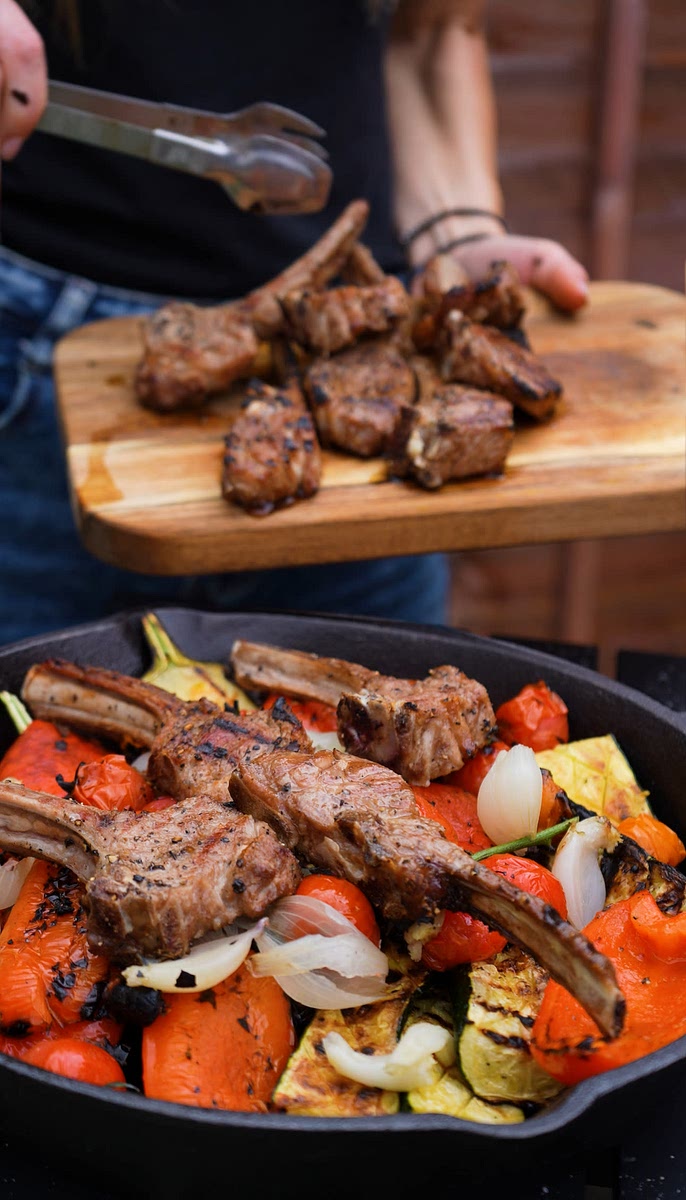 6. Transfer the vegetables to a greased large cast-iron skillet. Squeeze the shallots, peel the skin from the peppers, and arrange the lamb chops on top.