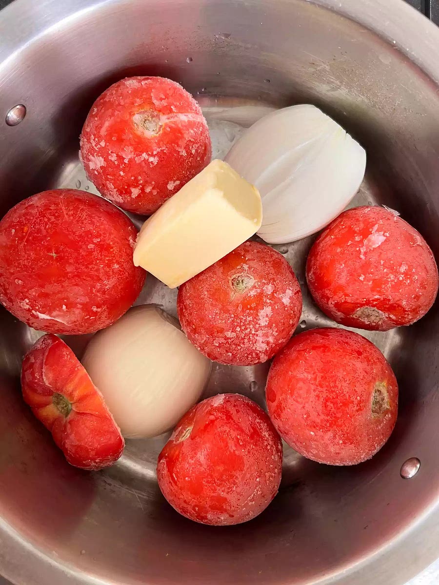place six large tomatoes (about 2 pounds), a yellow onion peeled and cut in half, and 5 tablespoons of salted butter in a pot. Because peeling and coring tomatoes is annoying, I don’t and it’s so good all the same. And if the tomatoes are frozen, I don't defrost them either