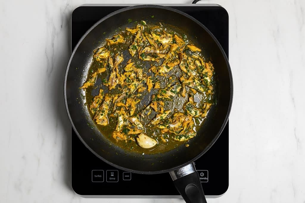 Passiamo al condimento: mettiamo in una padella un filo d'olio, lo spicchio di aglio intero. Lasciamo soffriggere un po’, e nel mentre tritiamo i pinoli. Poi togliamo l'aglio e aggiungiamo in padella i pinoli tritati, le sarde tagliate e la punta di concentrato di pomodoro.