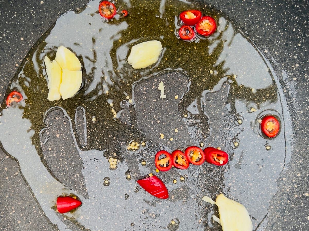 2. Pour a generous glug of extra virgin olive oil into the pan. Add 3 cloves of garlic slightly flattened and crushed using the flat of a kitchen knife, and the dried red pepper flakes (we used fresh chilli from our garden in this photo simply to use them up). If you are using ‘Nduja instead, add this now. Heat over a high heat until the garlic sizzles, but don’t let it burn and get bitter.