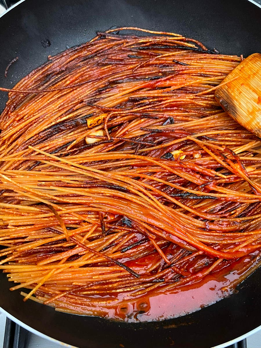 4. When the pasta has blistered and slightly burned on both sides, pour the passata into the pan. Add a little sugar if you are worried about the dish turning bitter. The passata will sizzle and start to simmer. Let it reduce without turning the spaghetti and listen carefully for the boiling point. When you hear it sizzle again (the noise changes sharply) remain patient and wait for sauce to start to catch on the base of the pan (this will take 30 seconds to 1 one minute). When it does, leave it for another 30 seconds or a minute. Then flip the spaghetti over, and leave it to catch on the base of the pan again (another minute or so).