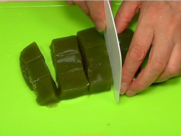 Inumidite un raschietto da impasto per evitare che si attacchi e tagliate i mochi al té matcha in cubetti.