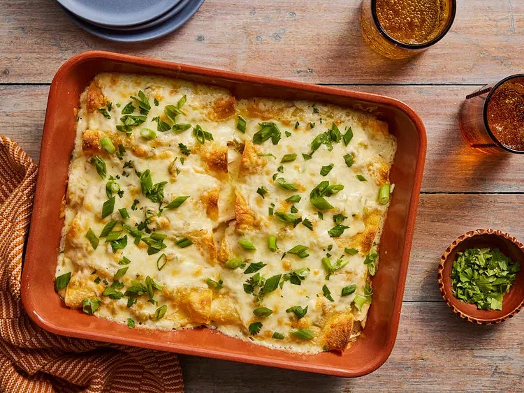 Preheat the oven to 375 degrees F (190 degrees C). Grease a 9x13-inch baking dish. Heat 2 tablespoons oil in a skillet over medium-high heat. Fry tortillas (one at a time) for 5 seconds on each side to soften and make them pliable. Add more oil to the pan as needed. Drain between layers of paper towel and keep warm. Divide chicken, 10 ounces Monterey Jack cheese, and onion among 12 tortillas. Roll up each tortilla and place seam-side down in the prepared pan. Melt butter in a saucepan over medium heat. Add flour and whisk until mixture begins to boil. Slowly add chicken broth, stirring with a whisk until thickened. Mix in sour cream and green chiles, stirring occasionally. Heat thoroughly but do not boil. Pour mixture over enchiladas. Bake in the preheated oven until bubbly and heated through, about 20 minutes. Top with remaining Monterey Jack cheese and bake for 5 more minutes. Garnish with chopped green onions and cilantro.