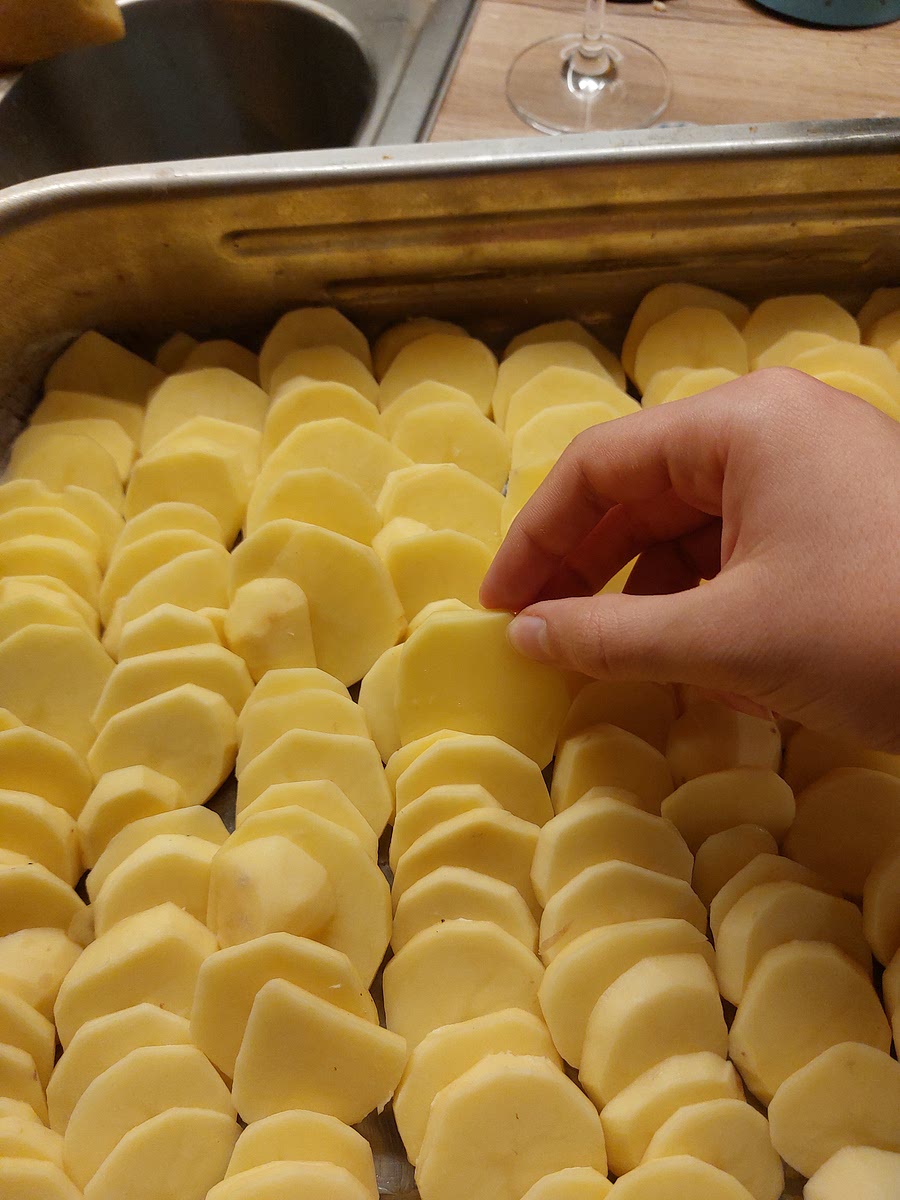 Die Kartoffelscheiben dachziegelartig schräg in die vorbereitete Form einschichten