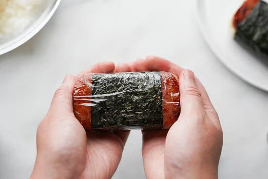To make a tighter musubi, cover the musubi in the cling-wrap again and twist both sides until it’s tight. You can also now use your hands to cup the sides and mold the shape so that it’s round.