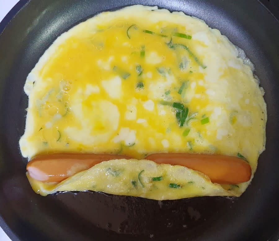 후라이팬에 식용유를 넉넉히 두른 후 계란물을 부어주세요. 그리고 아랫부분이 살짝 익을 때까지 기다려 주세요. 계란이 살짝 익기 시작하면 썰어 놓은 소세지를 길다랗게 넣어주세요. 그리고 조금 더 익었을때 계란으로 말아주기 시작합니다.