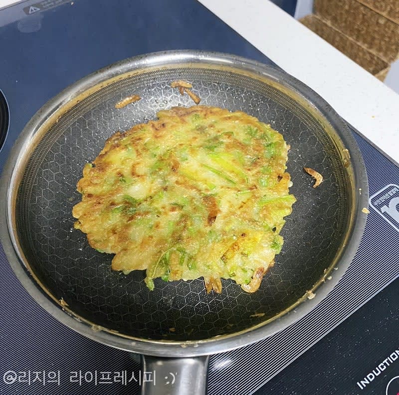 전 밑부분이 노릇노릇해지면 건보리새우 한줌을 위에 뿌려주세요. 잘 구워지면 전을 뒤집어주고, 식용유 한바퀴를 둘레에 돌려 같이 구워주세요