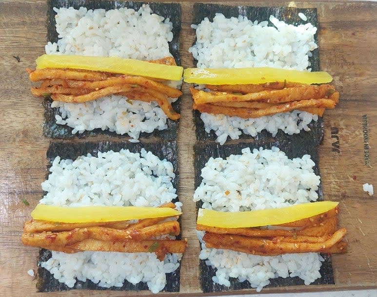 김밥김의 거친 면이 위를 향하게 한 뒤 밥을 얇게 펴 올리고 위에 매운어묵 볶음과 단무지 1개를 올린 뒤 손으로 꾹꾹 눌러 말아줍니다