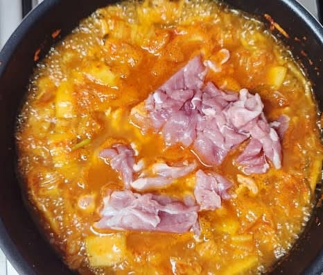 끓는 찌개에 돼지고기를 넣고, 다진 마늘 1 큰술, 고춧가루 1 큰술, 참치액 1.5 큰술을 추가하여 끓입니다.