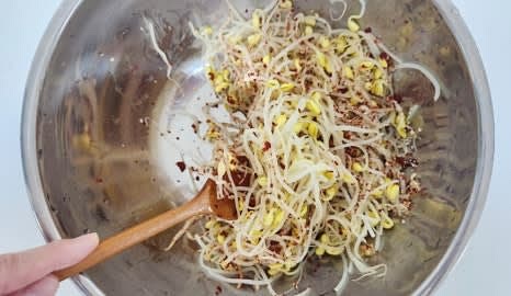 큰 볼에 식힌 콩나물을 넣고, 다진마늘 0.5 큰술, 소금 1 작은술, 고춧가루 1 큰술, 참기름 1.5 큰술, 깨소금 0.5 큰술을 추가합니다.