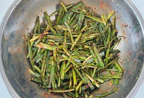 완성된 부추겉절이를 그릇에 담아 고기와 함께 곁들여 제공합니다.