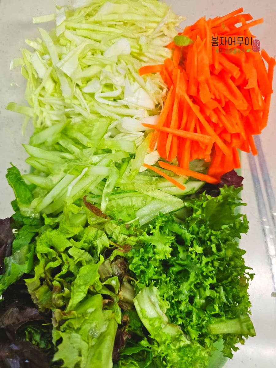 야채를 깨끗이 씻고 얇게 썰어 준비합니다. 오이는 소금으로 문질러 세척한 후 채 썰고, 양배추와 당근도 얇게 채 썹니다.