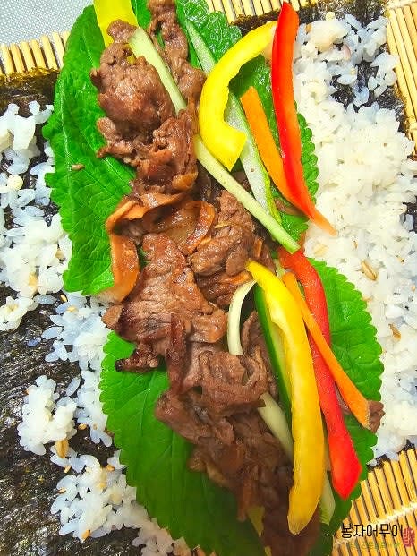 김밥 김 위에 밥을 고르게 펴고 깻잎, 단무지, 구운 불고기를 올려 돌돌 말아줍니다.