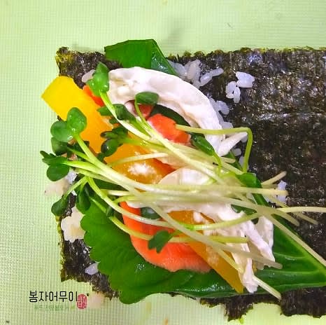 김 위에 밥을 골고루 펴고 깻잎 반만 잘라 올린 후, 훈제 연어, 단무지, 양파, 무순을 올립니다.
