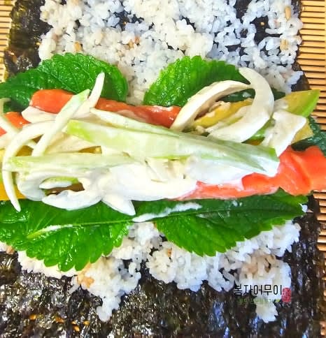 김 위에 밥을 얇게 펴고 깻잎을 올립니다. 깻잎 위에 단무지, 오이와 양파 소스 무친 것, 훈제 연어를 순서대로 올려줍니다.