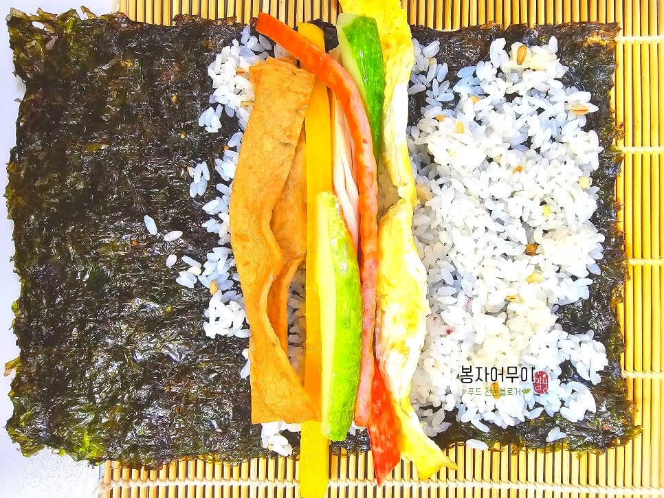 김 위에 밥을 펴고 준비한 재료(깻잎, 청양고추다대기, 계란부침, 어묵볶음 등)를 올려줍니다.