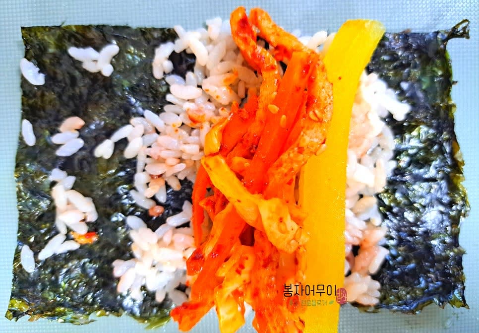 김 위에 밥을 얇게 펴고 볶은 어묵과 야채를 올려 돌돌 말아줍니다.