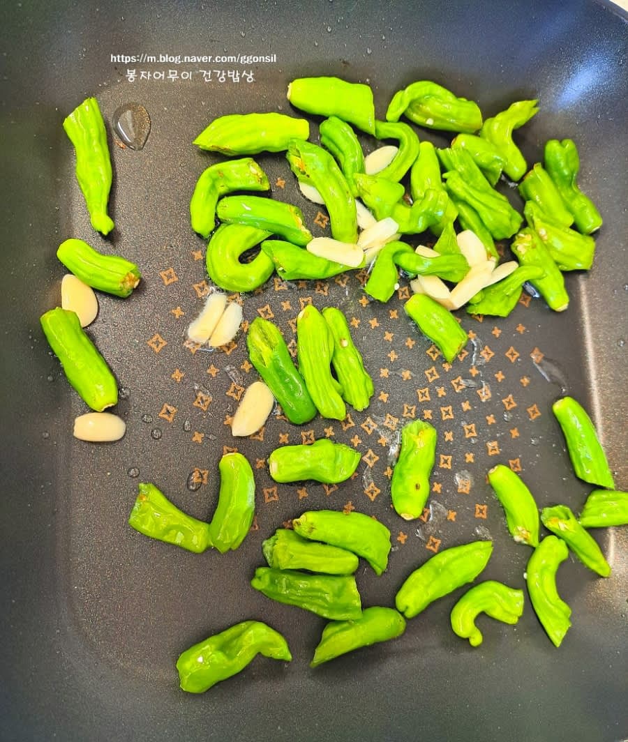 프라이팬에 기름을 두르고 약불로 달군 뒤 꽈리고추와 마늘을 먼저 볶습니다. 꽈리고추가 약간 숨이 죽으면 볶은 멸치를 넣고 섞어줍니다.