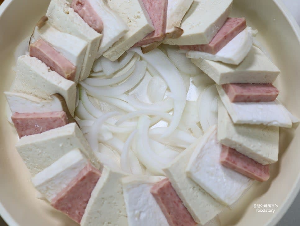 넓은 팬에 양파를 깔고 두부, 스팸, 새송이버섯을 순서대로 겹쳐 올립니다.