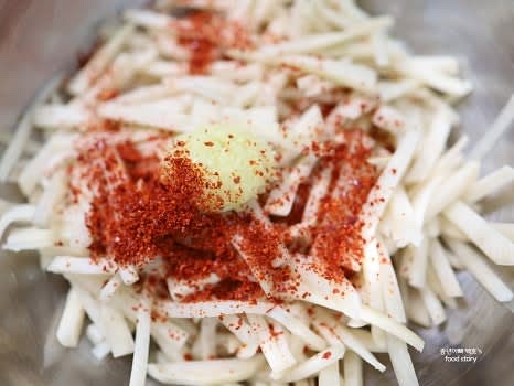 큰 그릇에 채 썬 동치미 무를 담고, 고춧가루 1스푼과 다진 마늘 1스푼을 넣습니다.