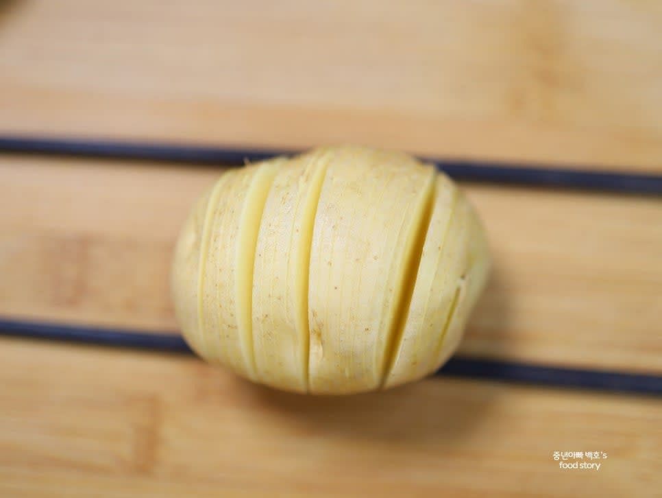 감자를 얇게 썰되 끝까지 자르지 않고 아래쪽에 나무젓가락을 놓고 썰어 붙어 있도록 합니다.