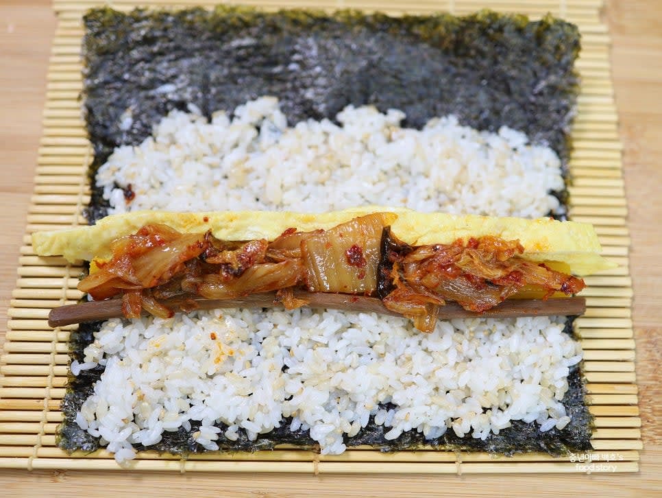 김발 위에 김을 올리고 밥을 얇게 펴 바릅니다. 중앙에 단무지, 계란지단, 우엉, 볶은 김치를 순서대로 올립니다.