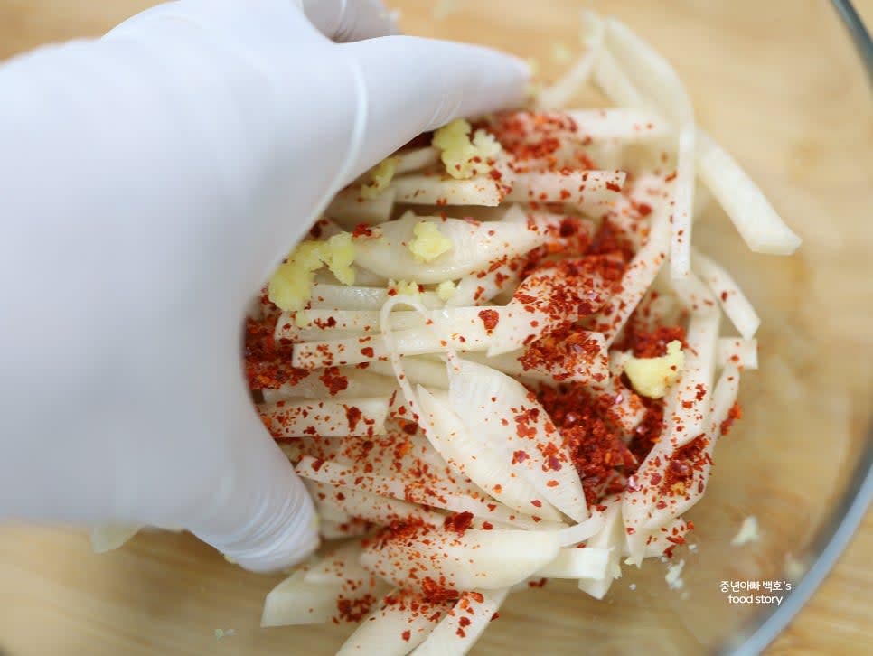 넉넉한 그릇에 썬 무를 담고 다진 마늘 1/2스푼과 고춧가루 1/2스푼을 넣고 골고루 무쳐줍니다.