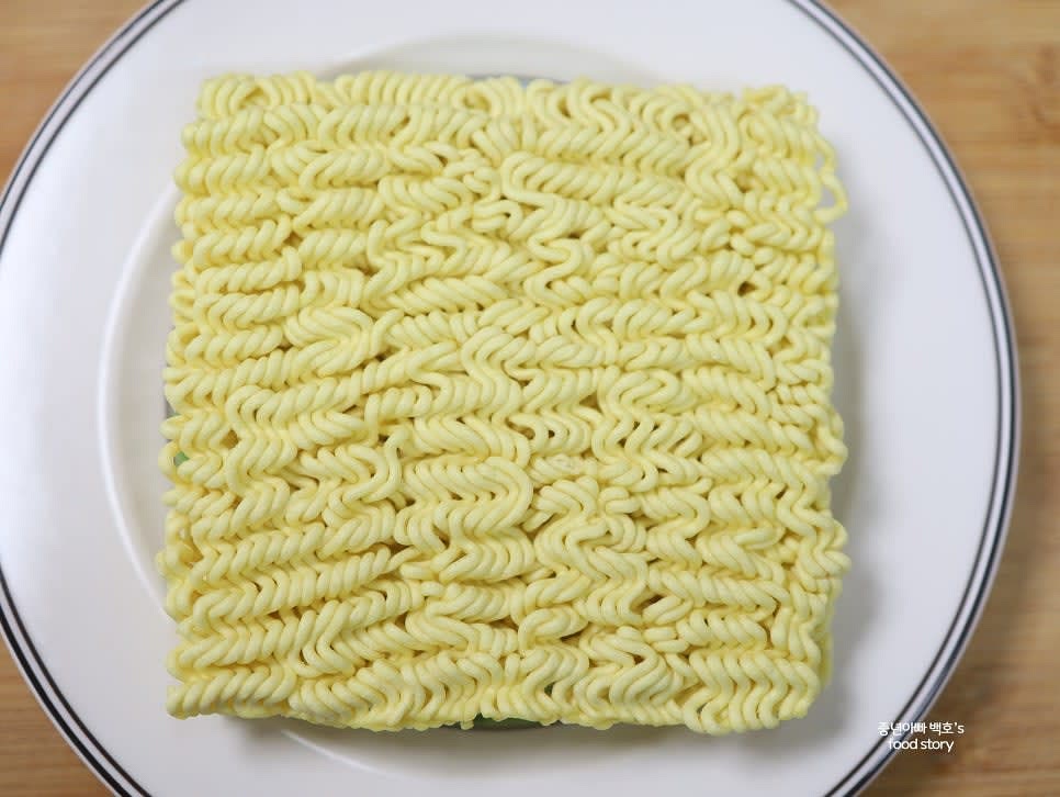 라면을 꺼내어 편평한 면이 위로 오게 접시에 놓습니다. 전자레인지 사용 가능한 접시를 사용하세요.