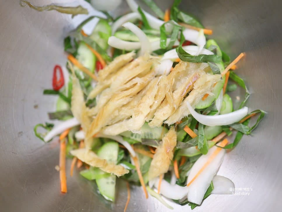 믹싱 볼에 양파, 대파, 오이, 당근, 깻잎, 황태채를 넣고 골뱅이 국물 1스푼과 다진 마늘 1/4스푼을 추가합니다.