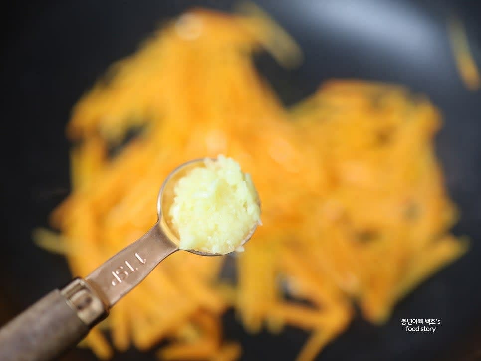 팬을 달군 후 식용유 2스푼을 넣고 당근채를 넣어 볶아줍니다. 색이 변하기 시작하면 다진 마늘 1티스푼을 넣습니다.