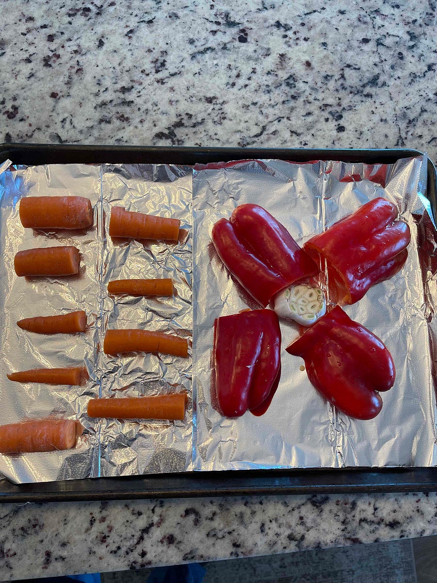 Slice off the top of the garlic, revealing the cloves. Cut the carrots into thirds and the peppers in half lengthwise.