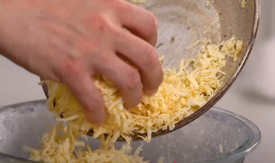 Gradually add the grated cheese while mixing, ensuring it is fully incorporated into the dough.