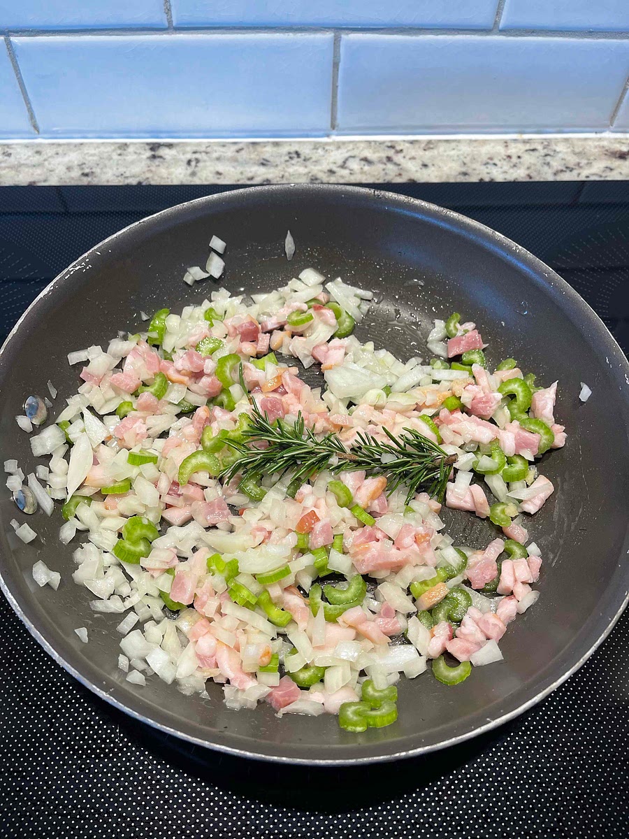 In a large skillet, melt the butter over medium heat. Add the diced bacon, onions, celery, garlic and rosemary sprig. Sauté until soft but not colored, about 10 minutes.