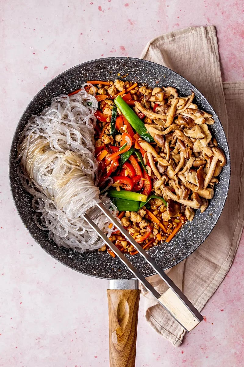 Nudeln und Pilze hinzufügen: Gekochte Nudeln und Pilze in die Pfanne geben. Mit einer Zange oder Stäbchen alles gut vermengen.
