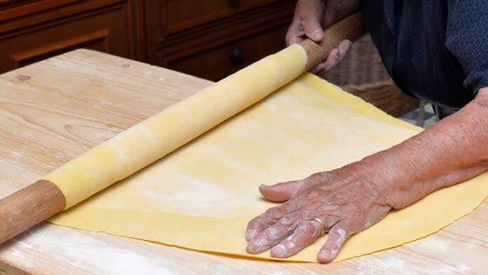 Uscire l'impasto dal frigo e procedere a stenderlo in modo MOLTO fine sul piano di lavoro (il risultato dovrà essere una sfoglia FINISSIMA di meno di 1cm, quasi trasparente se ci metti dietro la mano).
PRO TIP: Cerca di stenderla il più possibile, ma difficilmente senza la macchinetta riesci a farla sottilissima. Per questo, il trick che a me ha funzionato è: stendila il più possibile ora, ma, dopo che taglierai le singole tagliatelle, aprile una ad una, mettile una di fianco all'altra e passaci il mattarello di sopra. In questo modo, usciranno mooolto più sottili di come erano da appena tagliate.