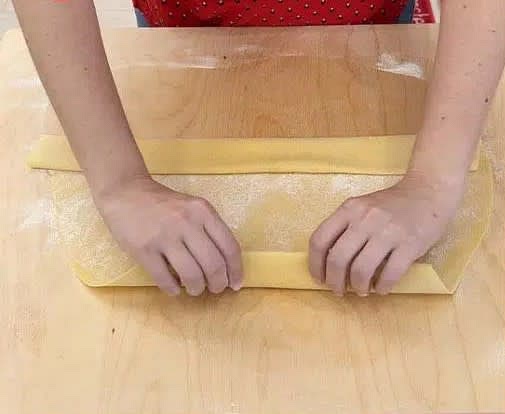 Una volta stesa tutta, prendi da uno dei lati lunghi e piegala per più volte su sè stessa fino al "centro" della sfoglia.
Fai lo stesso prendendo dall'altro lato lungo, e dopo unisci le due parti.