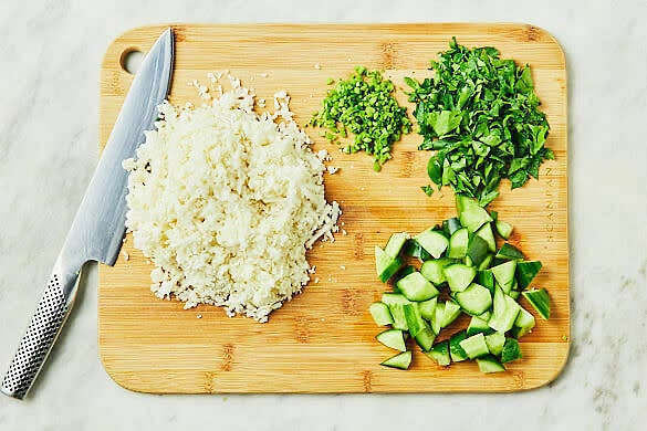 Coarsely grate the cauliflower (alternatively, process the coarsely chopped cauliflower in a food processor using the pulse button until it resembles rice). Coarsely chop the parsley leaves and finely chop the stems. Coarsely chop the cucumbers.