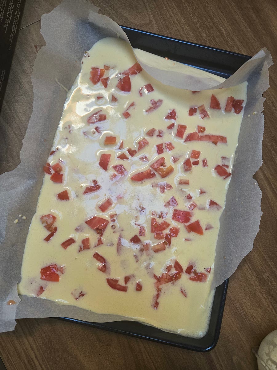 Sprinkle the omelet with mozzarella and about 2/3rds of the chopped tomatoes. Working from one of the shorter ends, and using parchment paper to help you lift the omlet, roll the omelet up tightly. Return it to the oven for another ten minutes to melt the cheese.