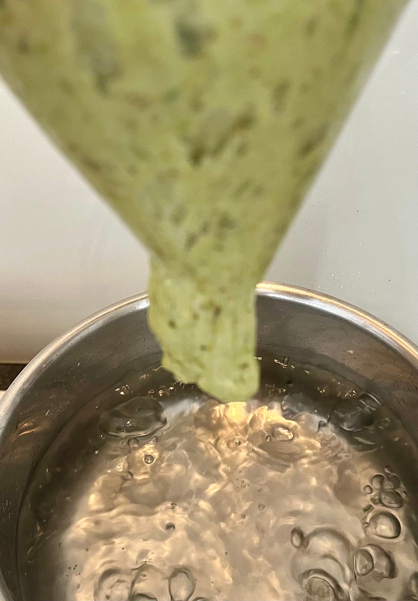 Once the 30 minutes wait for the dough have passed, remove the bowl with the dough from the fridge. Pour the sticky dough into a ziplock or similar plastic bag, remove the air from it and zip it closed. With a pair of scissors, cut a corner of the bag so you end up with a hole of about-1.5 cm diameter. Holding the bag in one hand and the scissors in the other. Carefully and slowly squeeze the bag over the pot so a string of dough starts coming out of the hole in the bag. Using the scissors cut the gnocchi so they fall straight into the boiling water. Try to cut them in similar sizes. Do this from close up to the surface to avoid splashing.
