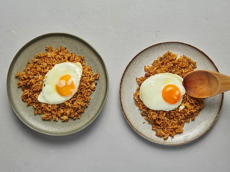 Divide rice between two plates and top each plate of rice with a fried egg. Garnish with cucumber and tomato slices and shower with fried shallots, if you like. Serve immediately with kecap manis alongside for drizzling.