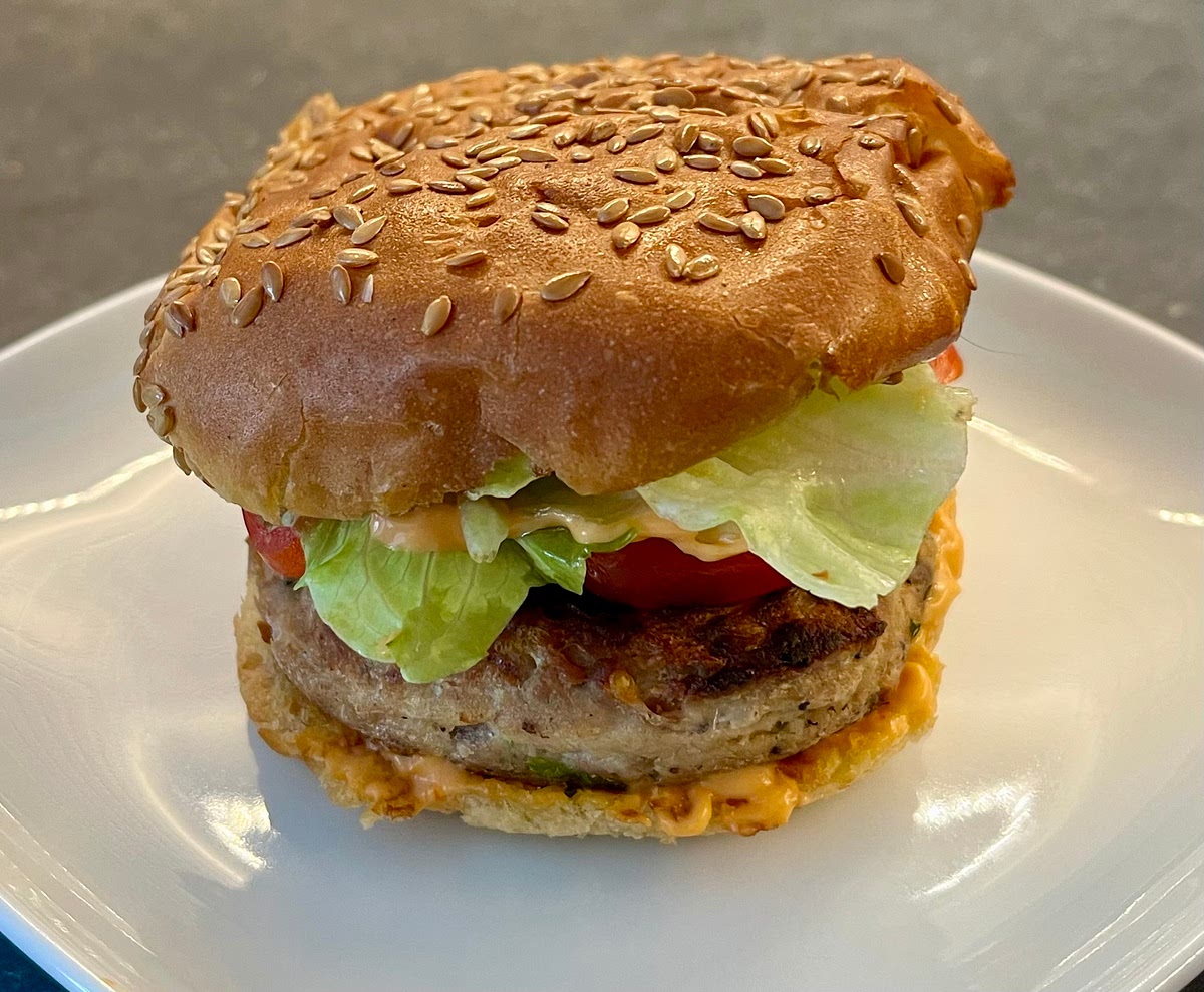 Once burgers are golden on both sides, put on the bun with the sriracha mayo, add the sliced tomatoes, the lettuce, dress them with a swirl of extra virgin olive oil and a pinch of salt, then cover with the seeded top of the bun and serve.