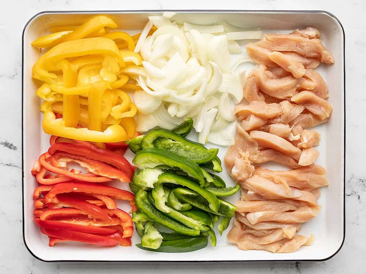 Cut the onion and bell peppers into 1/4- inch wide strips. Slice the chicken breast into thin strips. Add the chicken and vegetables to a large baking sheet or casserole dish.