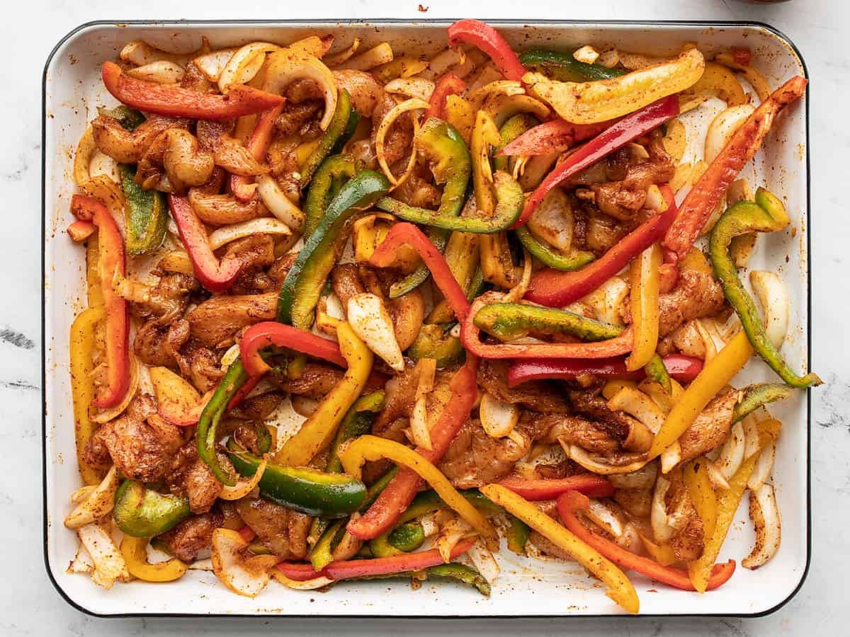 Drizzle the cooking oil over the chicken and vegetables, then sprinkle the fajita seasoning mix over top. Use your hands to toss the ingredients until everything is well coated in oil and seasoning. Spread the chicken and vegetables out over the baking sheet evenly.