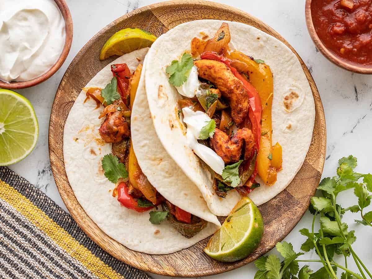 To serve, scoop a small amount of meat and vegetables into the center of each tortilla. Top with a few sprigs of cilantro, a dollop of sour cream, and an extra squeeze of lime if desired.