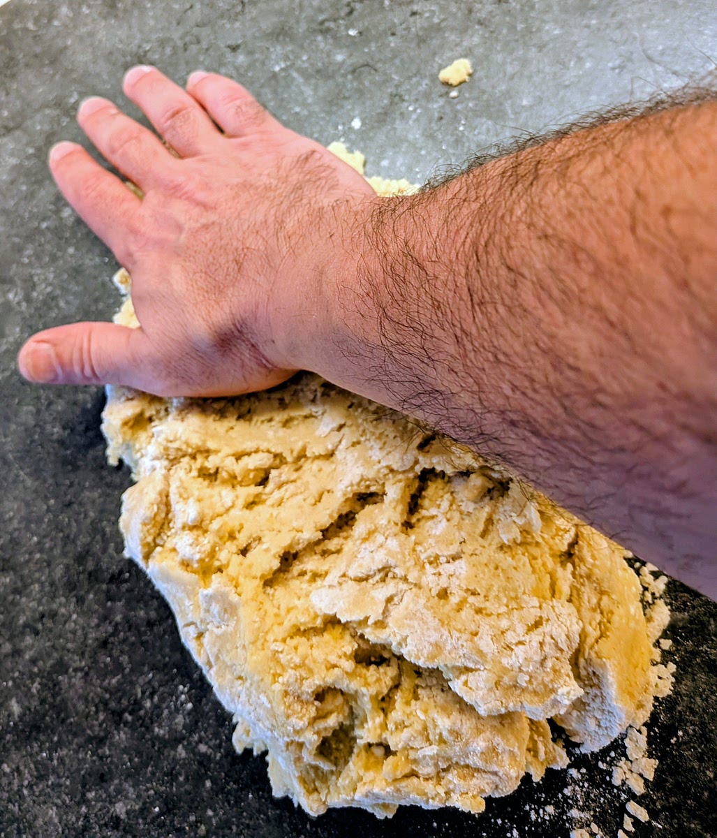 Pour the pastry mix on a working surface. Don't knead it hard, just push and drag bits of it, stretching it against the surface using the palm of your hand, just enough to integrate the flour that has not yet joint the mix. Should take one or two goes over the dough to integrate all of the flour; don't do this for more than 3 times. Don't overwork or overheat the dough with your hands, as this will develop the gluten and affect the texture and finish.