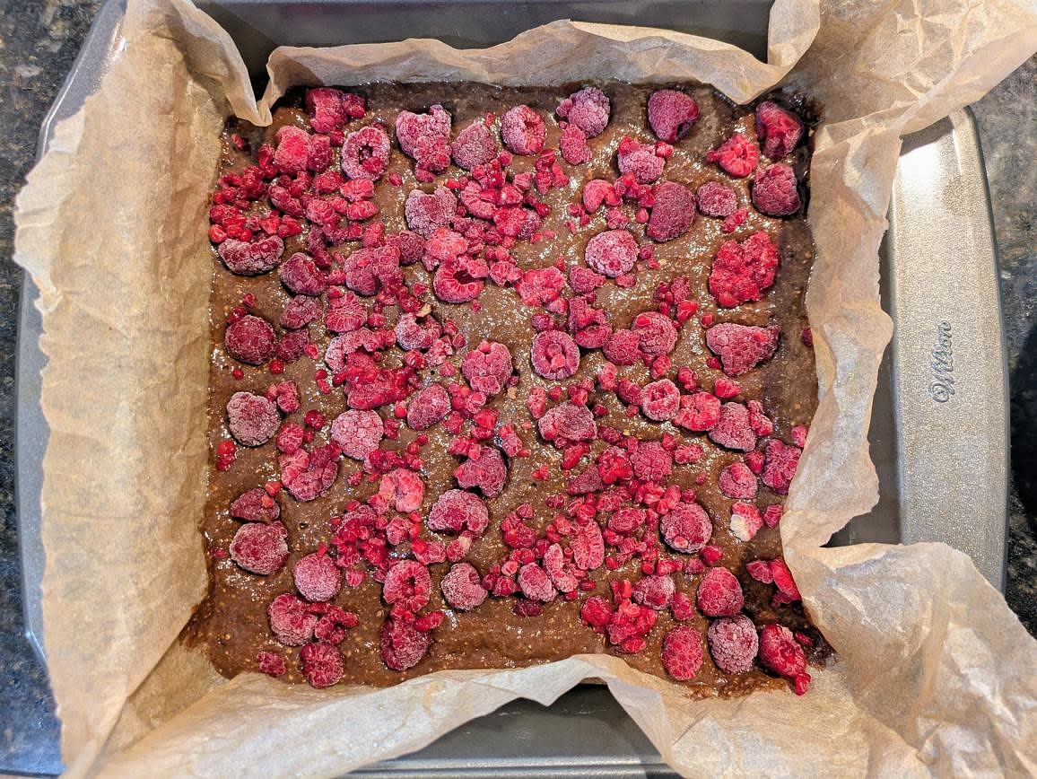 Transfer the batter to your parchment lined pan, and top with your raspberries, lightly pressing them into the batter